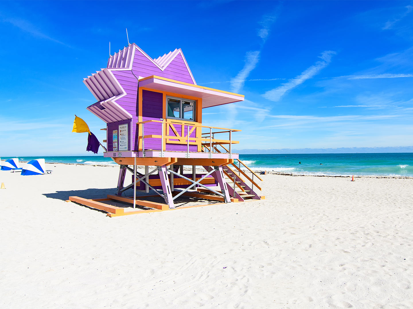 A purple lifeguard station on a beach with white sand and a blue ocean in the background.