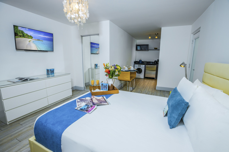 A wide view of a hotel suite with a large bed, kitchenette, and flat screen TV.