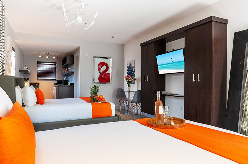 A wide view of a hotel suite with two beds, a kitchenette, and a dining area.