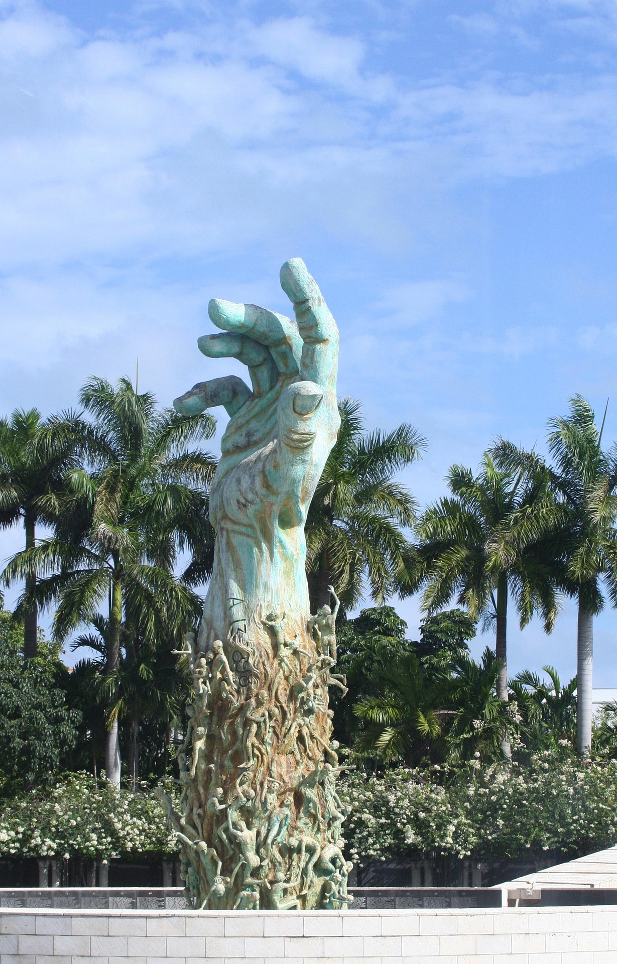 A large sculpture of a hand reaching up towards the sky, surrounded by smaller figures and palm trees in the background.